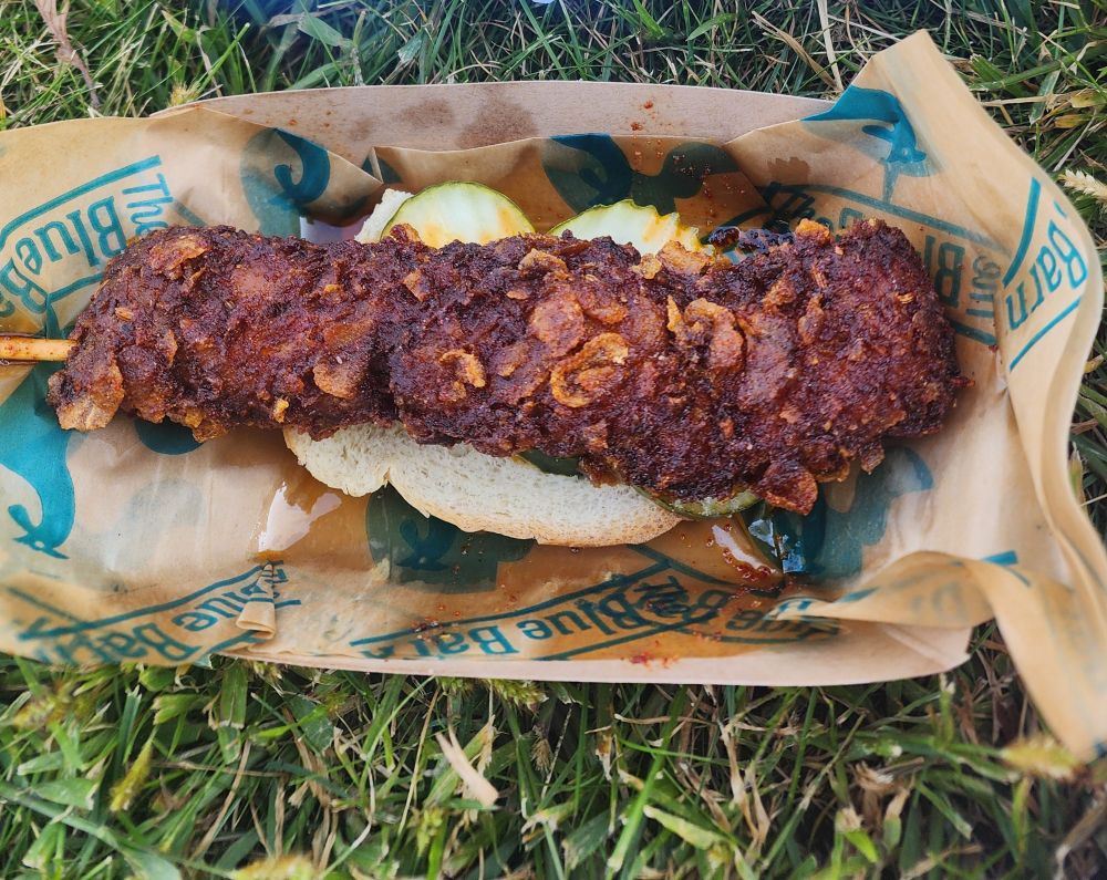 picture of a piece of hot fried chicken on a stick on top of bread and slices of pickles