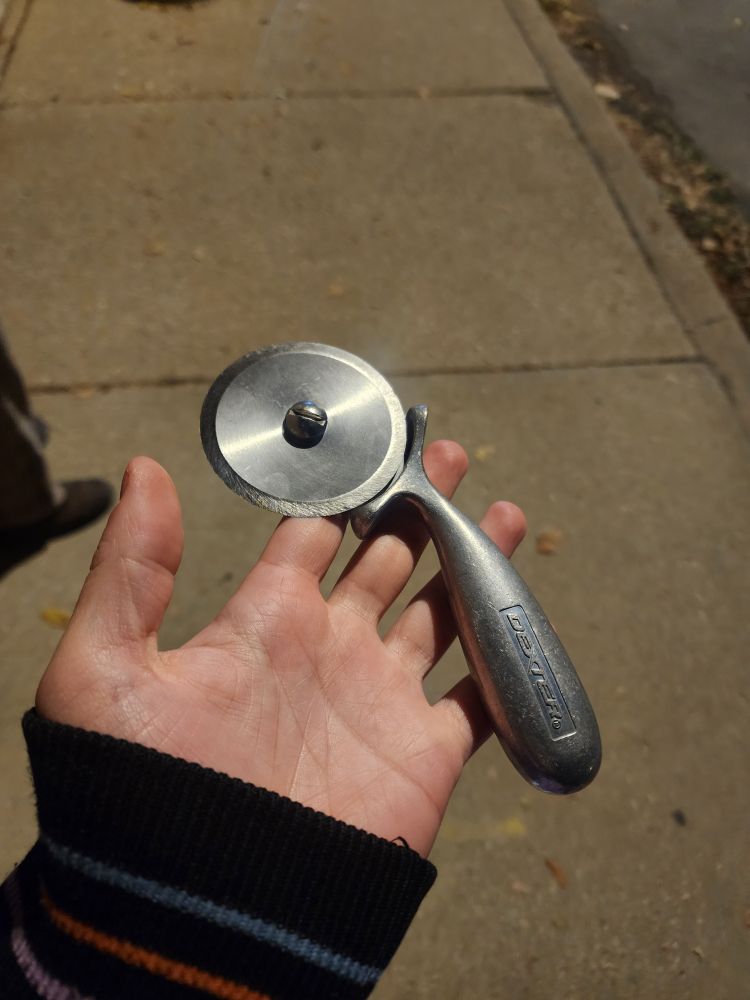 picture of juni's hand holding a thick metal pizza cutter