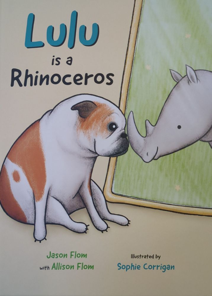 A book cover of 'Lulu is a Rhinoceros' showing a white bulldog with brown patches with her nose pressed to the mirror looking at her reflection showing a gray smiling rhino.