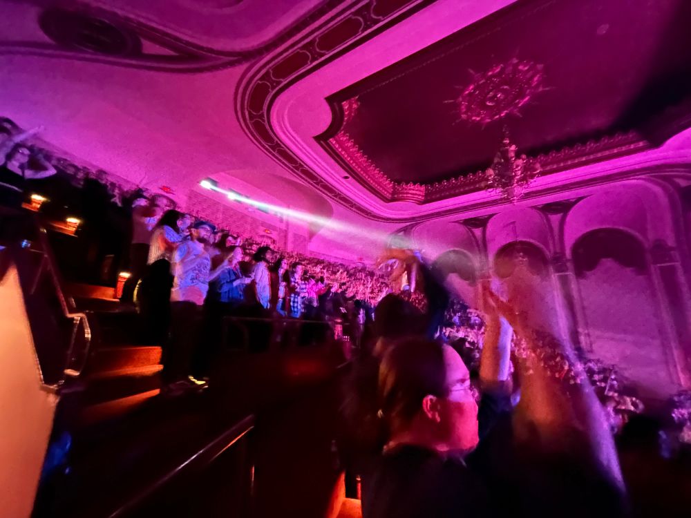 Wide angle shot facing up in a theater of people clapping and having their hands up