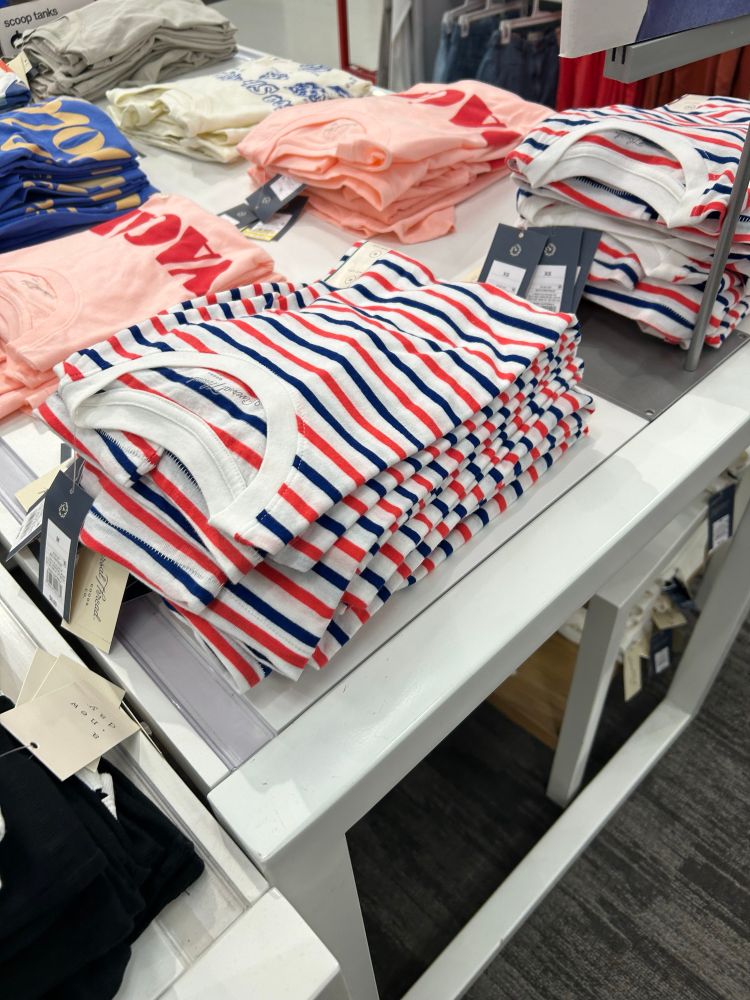 Red white and blue striped shirt folded with two other graphic tee designs in view 