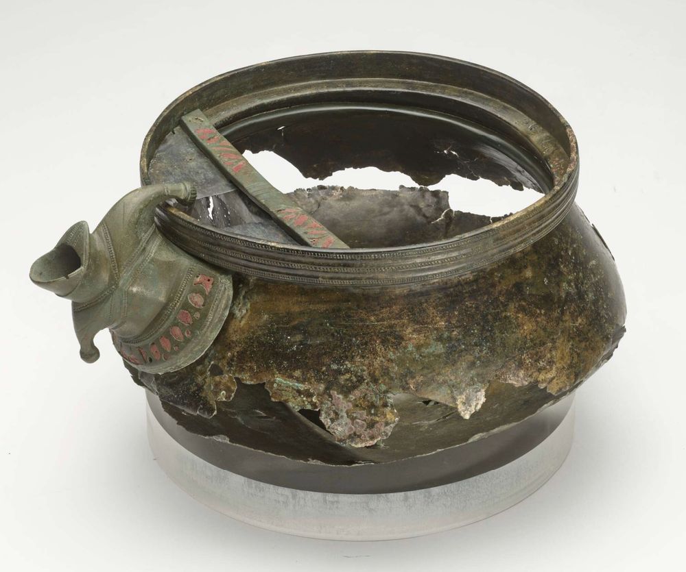 Photo of copper alloy shallow bowl with lid and spout fitting, with red enamel deocration. The spout looks vaguely anthropomorphic. 