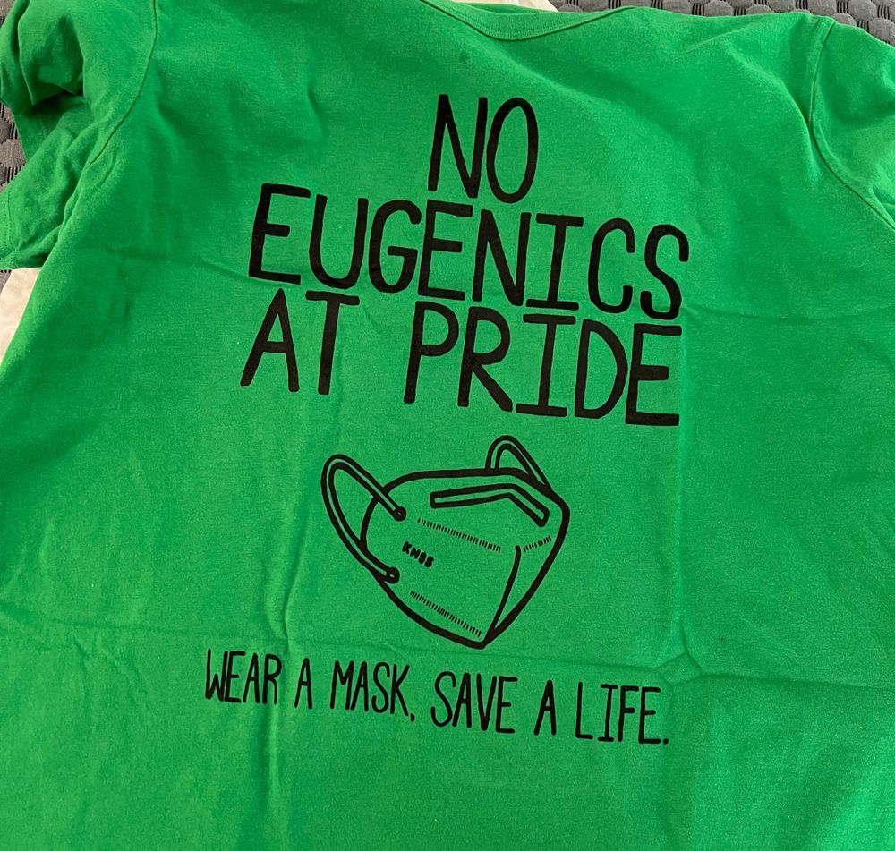 Green screen printed shirt that says no eugenics at pride, and shows a KN 95 mask. Shirt and design is by A’lece Moore.