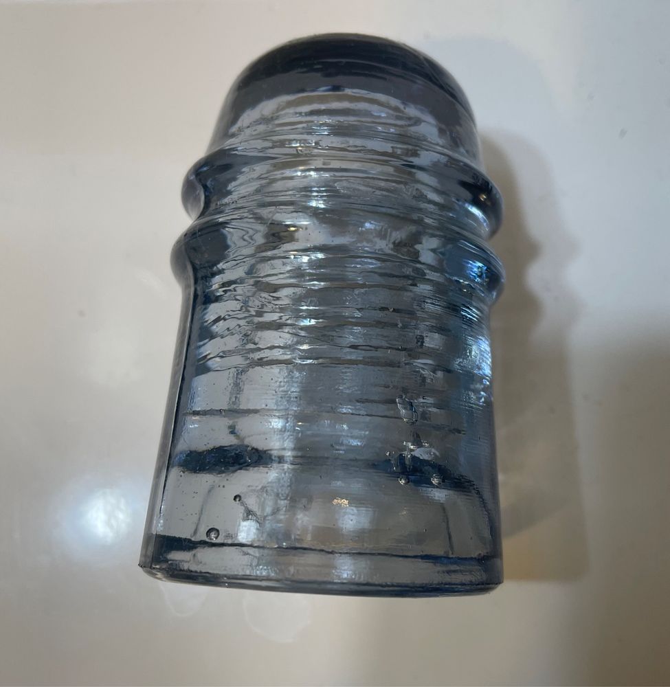 Slightly purple-gray telegraph/telephone glass insulator, domed shape with a notch for holding the wire, grooves inside to screw it onto the telephone pole arm.
