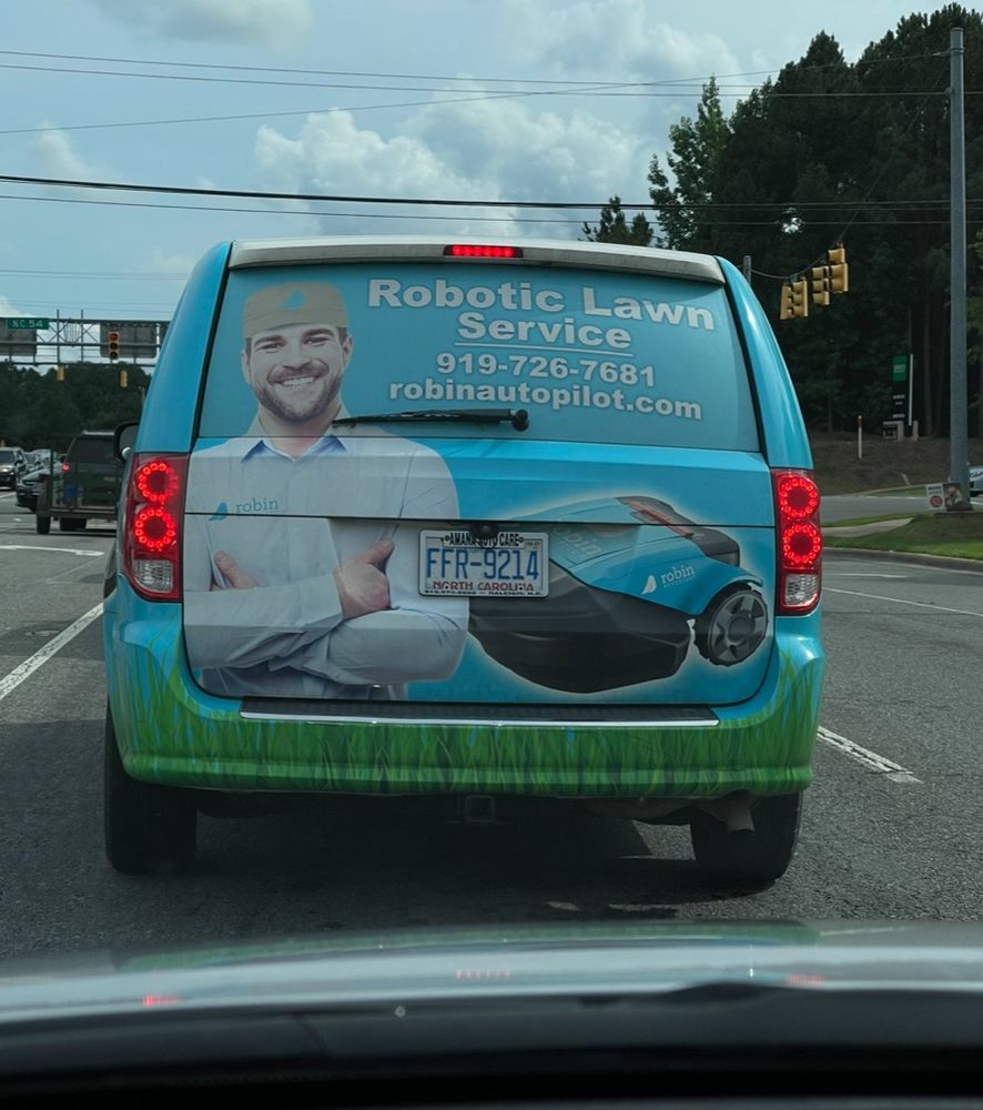 The rear of a work van that says robotic lawn service, and has a picture of a robotic lawnmower, next to a smiling person.