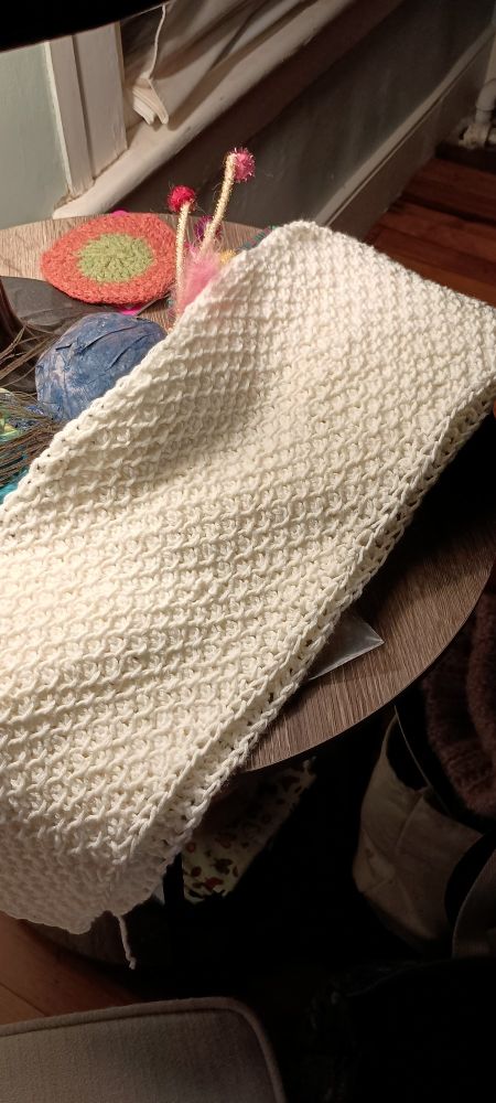 Hand crocheted scarf in cream drapes across a small table 