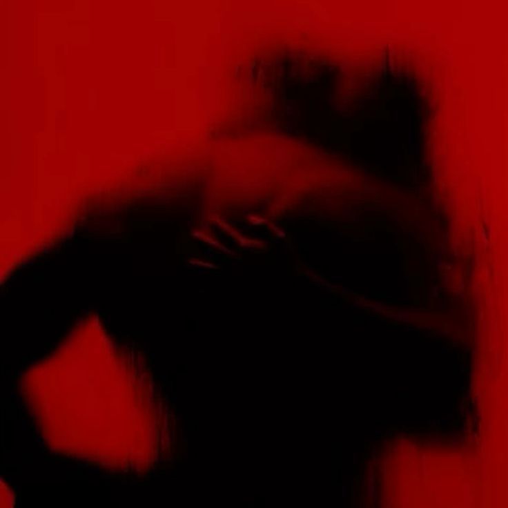 a red tinted image of a man and a woman gripping each other behind a fogged up glass. The mans back and shoulders prominent as the woman's hand can be seen splayed in the middle of his back. A blurred view of her face nuzzled into his neck. 