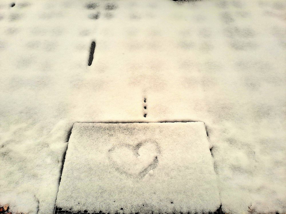 Boden meiner verschneiten Terrasse. In den Schnee auf der Fußmatte wurde ein Herz gemalt. 