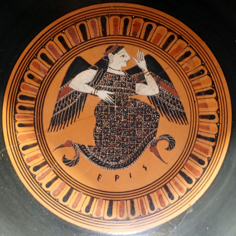 Ancient Greek ceramic plate artwork featuring the figure of Eris, the goddess of strife. The image is centered within a circular frame patterned with alternating black and ochre-red segments, resembling rays or stylized petals. Eris is depicted mid-stride in dynamic motion, suggesting running or swift movement. Her form blends human and mythic features: she has wings extending from her shoulders, a heavily patterned dress with X and dot motifs, and feet adorned with what resemble feathered shoes, emphasizing agility. One hand is raised in front of her face in a gesture that could signify speaking, signaling, or casting. The name “EPIS” is inscribed below the figure in ancient Greek letters, identifying her. The overall style is black-figure pottery, characteristic of Attic vase painting.

Generated with BSky AltText CustomGPT.

