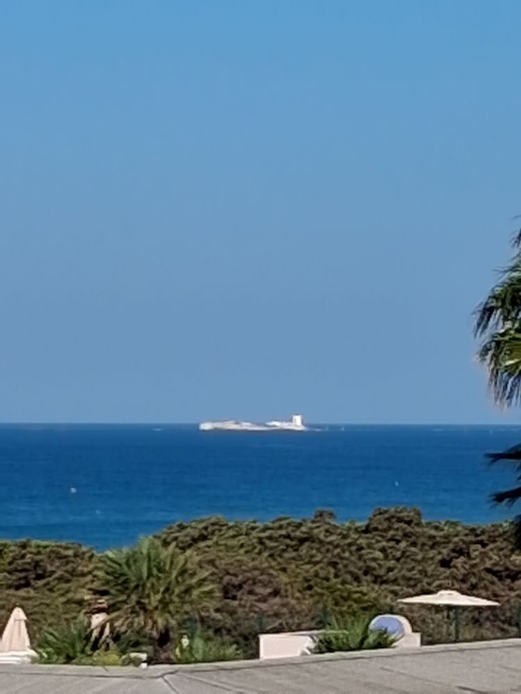 Im Vordergrund grüne Dühnen, dahi,ter dunkelblaues Meer. In der Ferne eine weiße Inselfestung