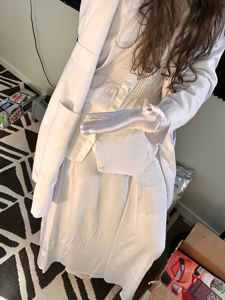 an all-white outfit - skirt, blouse, lab coat, gloves - with a hole at the front of the thumb of a glove.