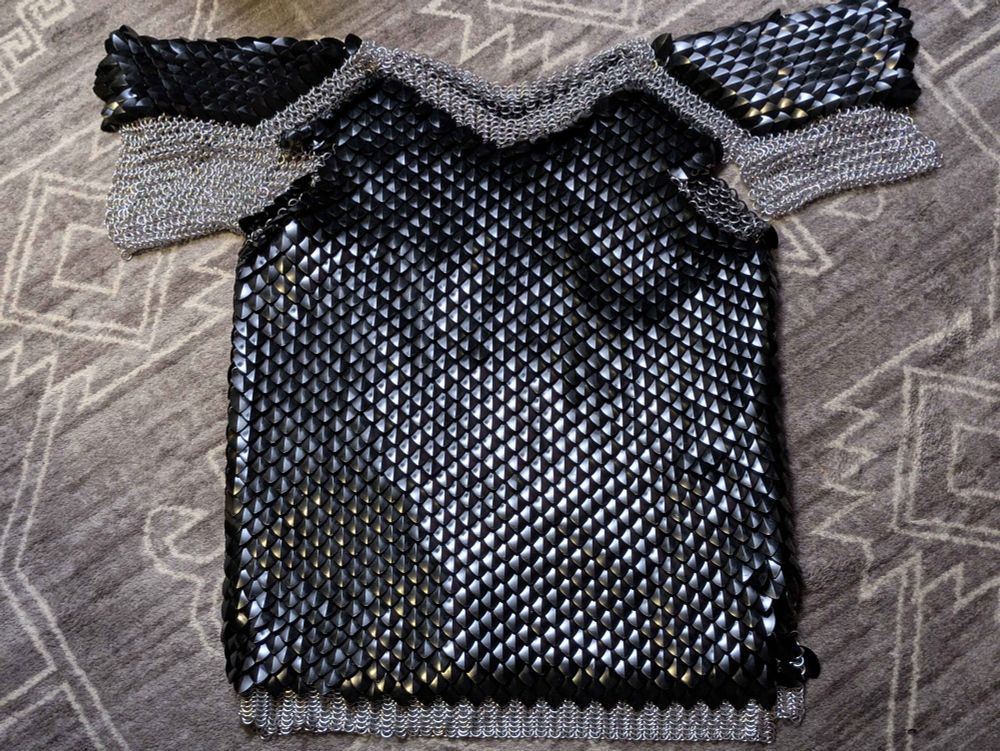 A picture of a shirt constructed out of bright aluminum jump rings and plastic dragon scales in the style of chainmaille/scalemaille laying on a rug. showcasing that it was the biggest pain in the ass thing i have ever crafted with my own two hands and they're absolutely screaming and i need a damn break, but can't take a break yet....i scream. 




a!