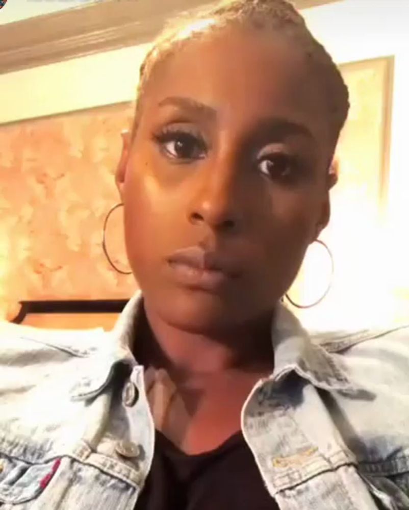 a woman wearing a denim jacket and hoop earrings is making a face .