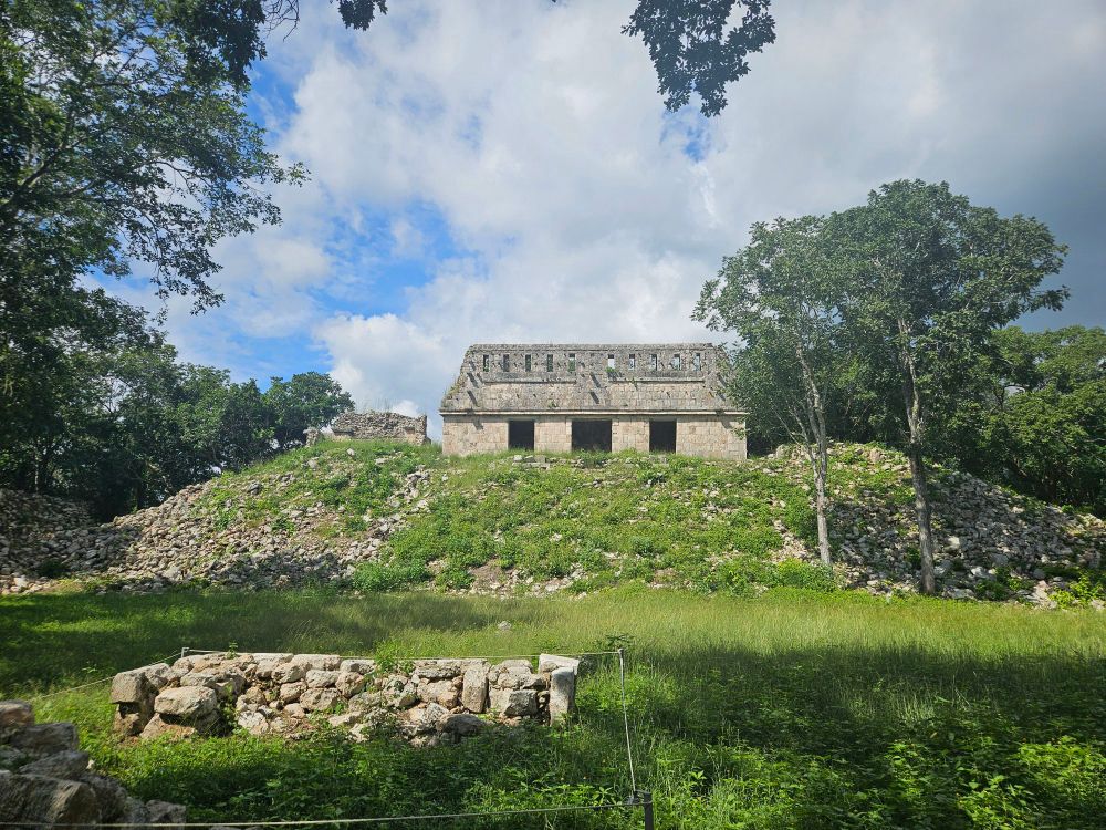 Blick auf einen grünen Hügel, im Dschungel, mit einem alten Gebäude aus Stein aus der Mayazeit.