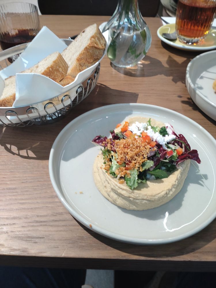 Bread basket with a plate of hummus. Dressed up with arugola, lemon zest, paprika chucks and something crispy bits what I don't know what it is.