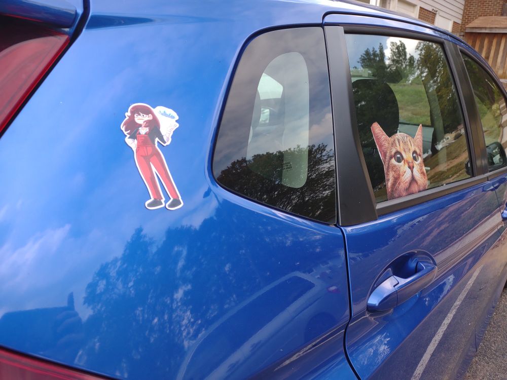 Dumbing of Age Book 13 Kickstarter Carla with Pie magnet on car, guarding window with realistic orange tabby "cat peeking" sticker (one ear torn from vandals to look like a TNR capture)