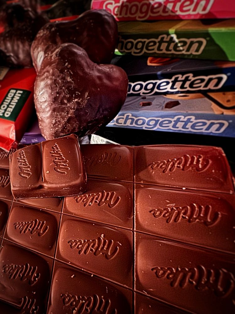Eine ausgepackte Tafel Schokolade im Vordergrund, dahinter mehrere Tafeln in der Verpackung. Dazwischen liegen Schokoladenherzen.