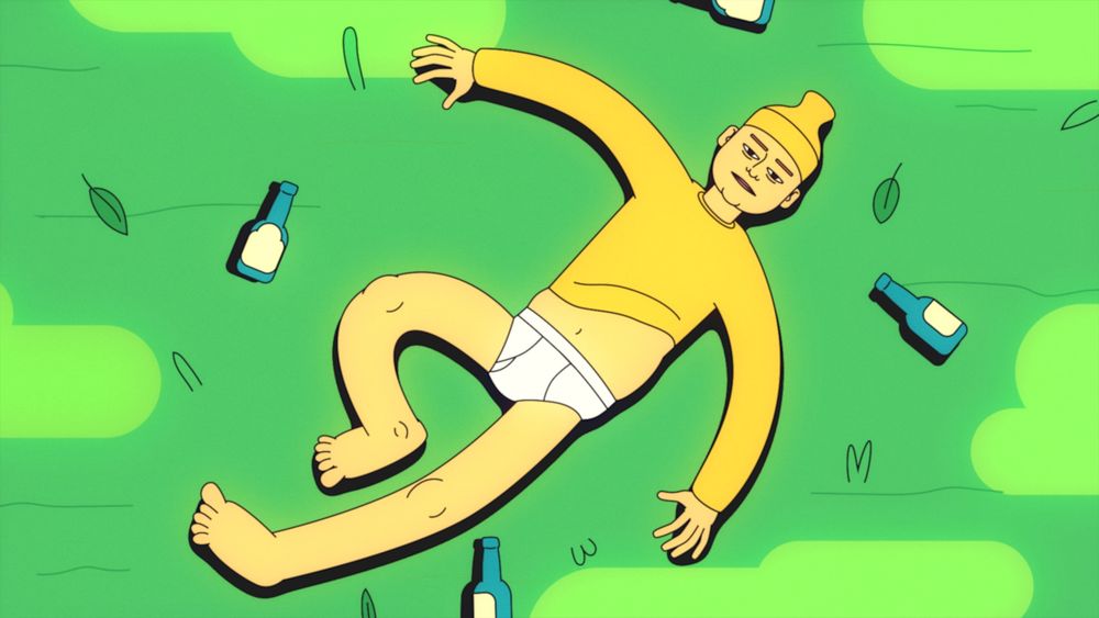 Matt Batey dressed in yellow sweatshirt and yellow beanie lies in his underpants in a field surrounded by empty alcohol bottles.