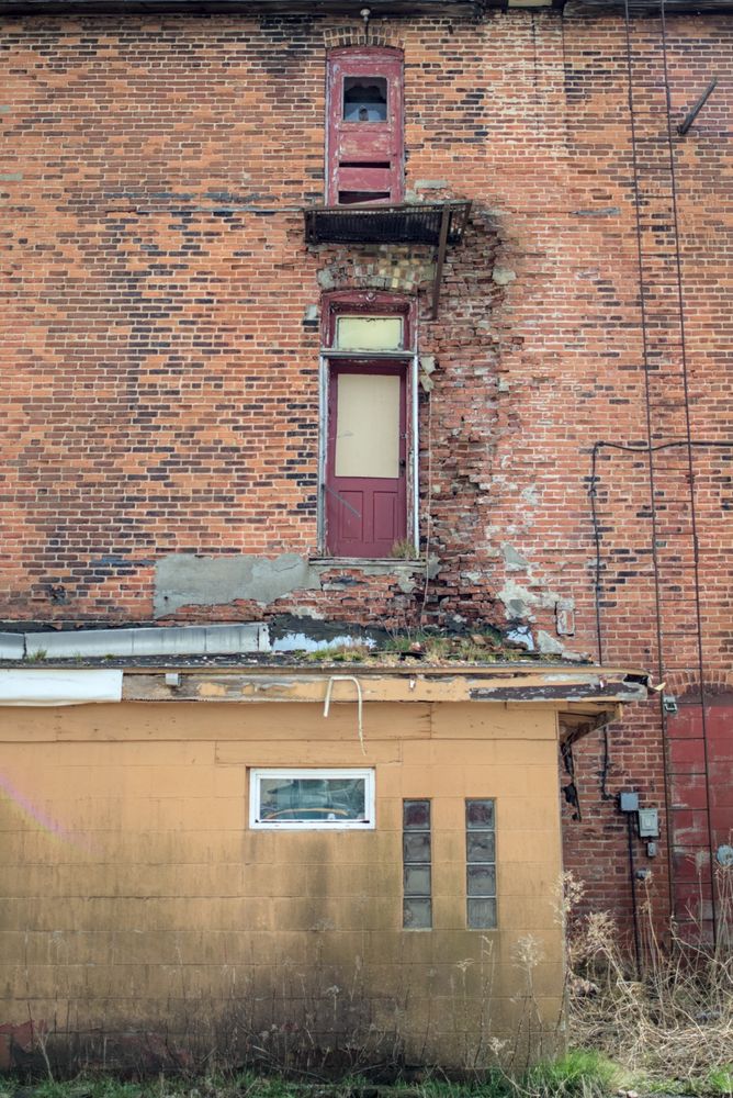 Red doors in weathered brick  – Two stacked red-painted doors (one upper-level with no balcony) set into a worn red brick wall above a mustard-yellow exterior.