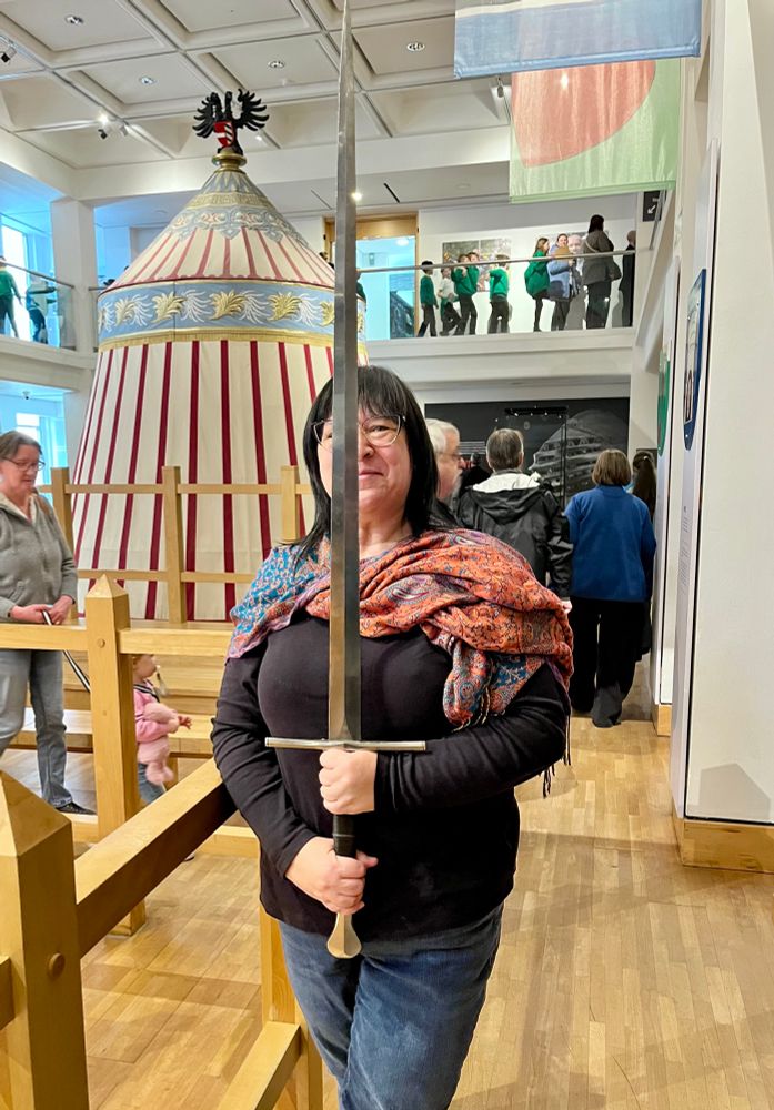 A dark haired woman holding a sword vertically in front of her.