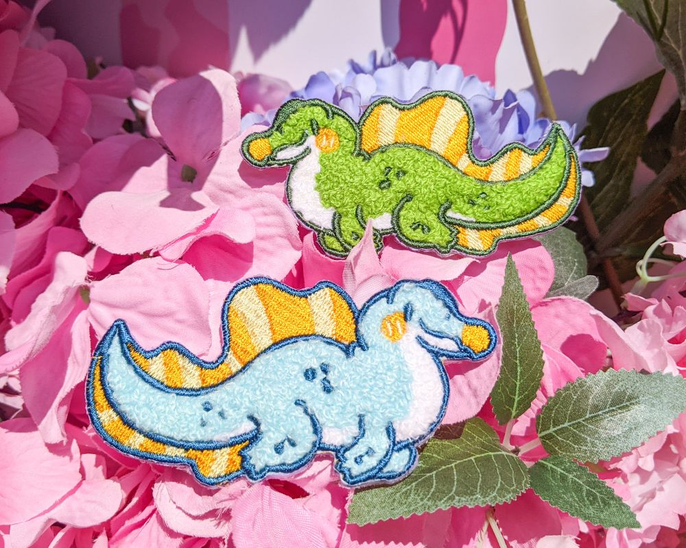 Photo of fuzzy green and blue spinosaurus patches against some pink artifical flowers