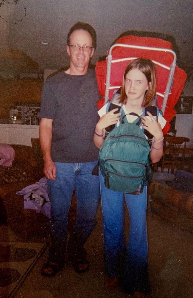 old, decaying print of a photo. my father and i stand in our living room. i have a hikers backpack on my back with a regular backpack on my front, and a strange expression. i am about 11 or so i think here. my dad is standing next to me, a proud smile on his face 