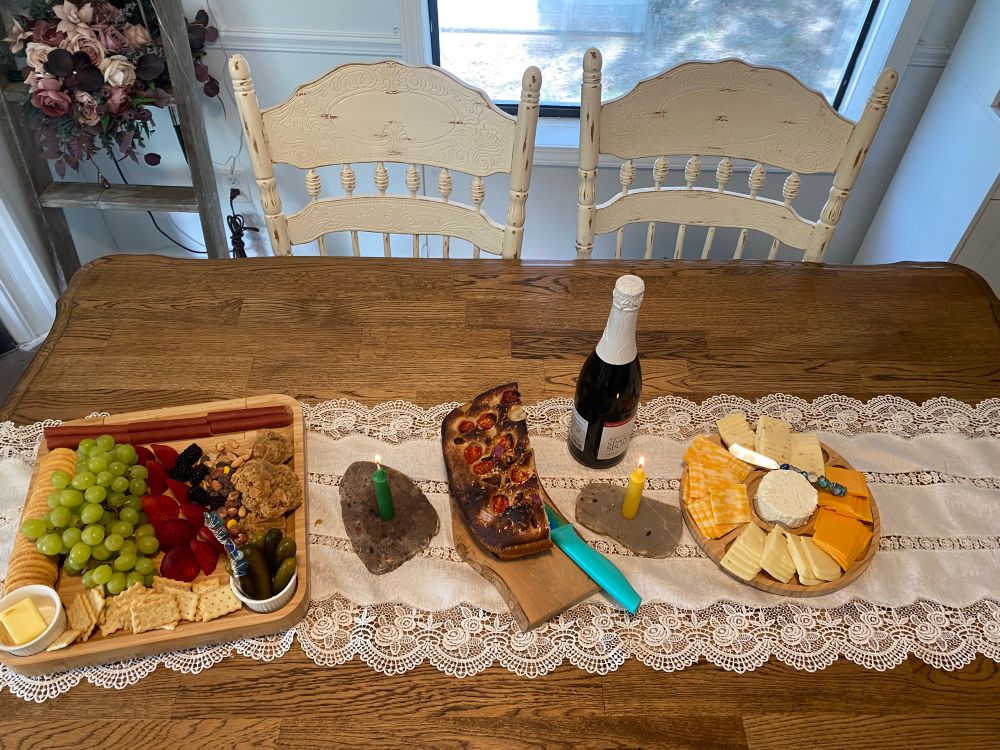 A great spread of cheese , fruits and sparkling supmante , along with focaccia and candles 