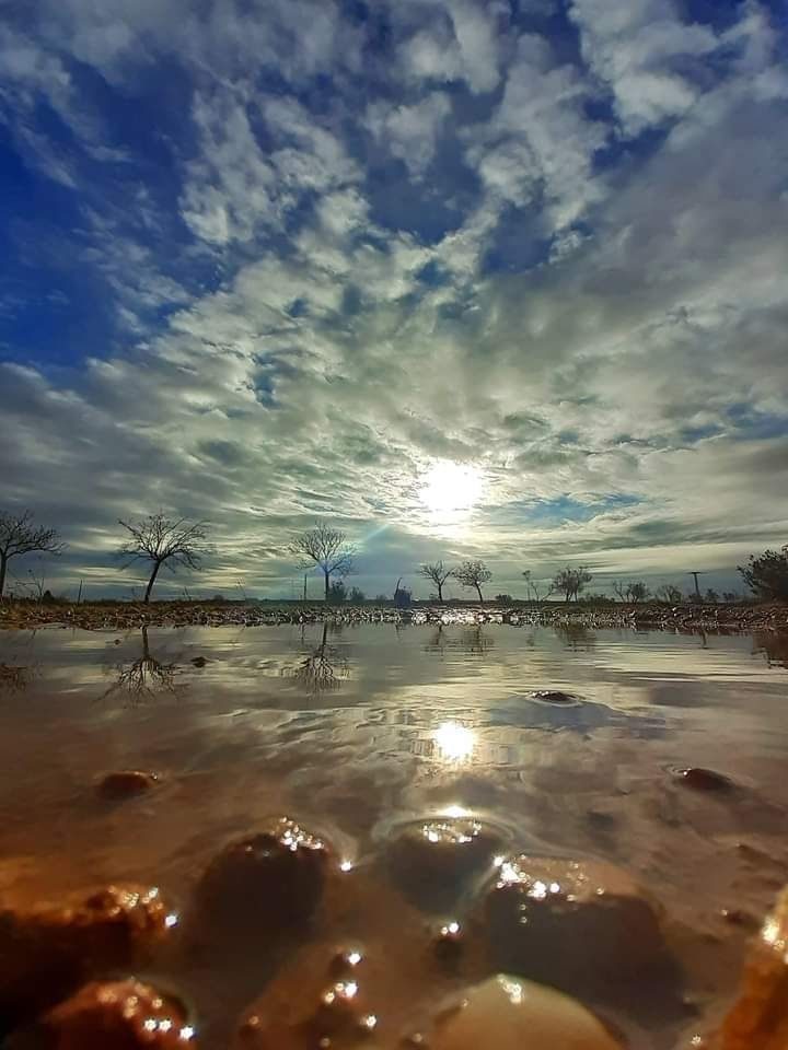 Se ve el cielo con nubes que dejan pasar la luz  del sol reflejado a su vez en un charco creando un efecto infinito.
