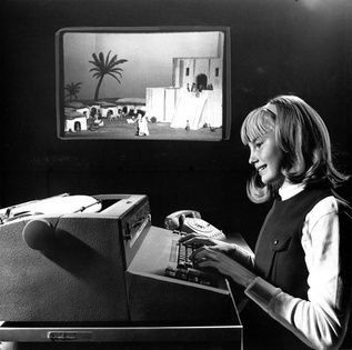 A black and white photo of a student in 1966 playing The Sumerian Game, the first 'video game' with writing designed by Mabel Addis. It was a text-only game that printed out everything on a typewriter kind of device.