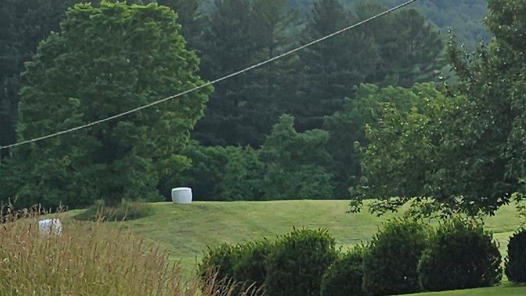 A landscape shot of a gently rolling green mown field with a couple of plastic wrapped large round hay bales that look like giant marshmallows 