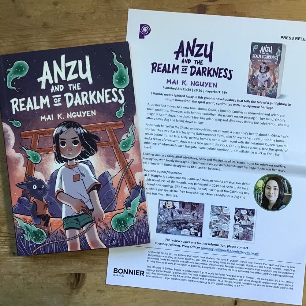Copy of Anzu and the Realm of Darkness by Mai K. Nguyen showing a girl armed with a bow and arrow and a dog-like creature both in front of a torii, with fantastical tadpole-like creatures flying around them. Also included is the book’s press release. 