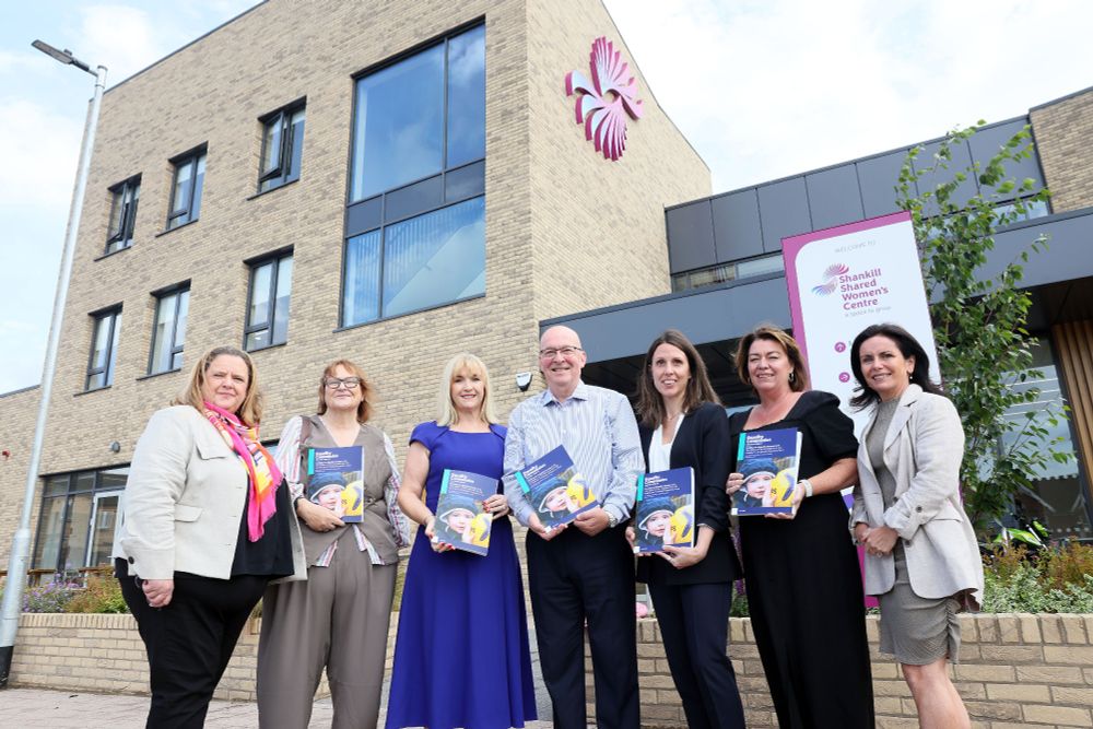 Seven people standing in front of the Shankill Shared Women's Centre, with some holding a research report titled 'Funding for Equality Groups in NI: The Impact of the Transition from EU Funding to UK Shared Prosperity Fund'