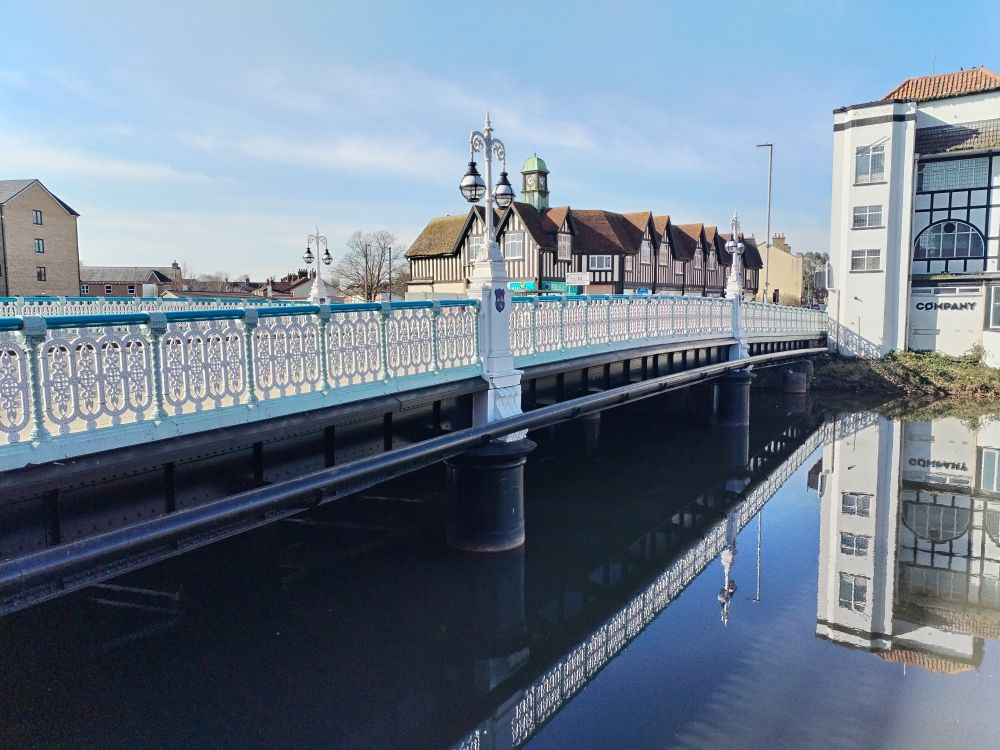 Bridge in white and blue wrought iron work, reflected in the river Tone, along with the very blue sky