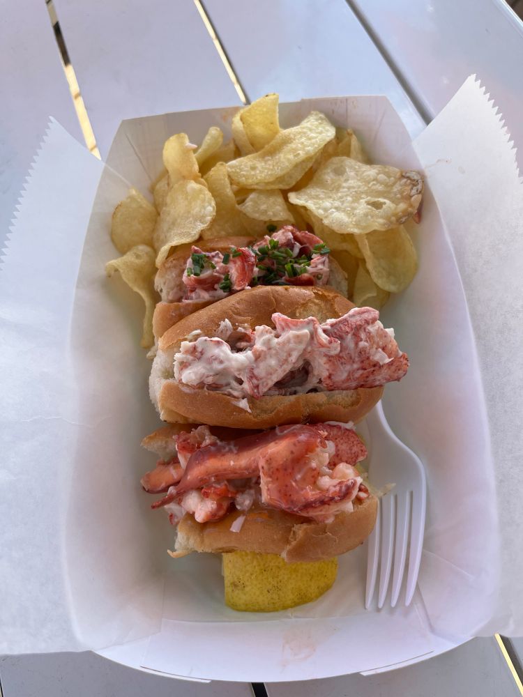 Three small lobster rolls and potato chips in a paper takeout basket