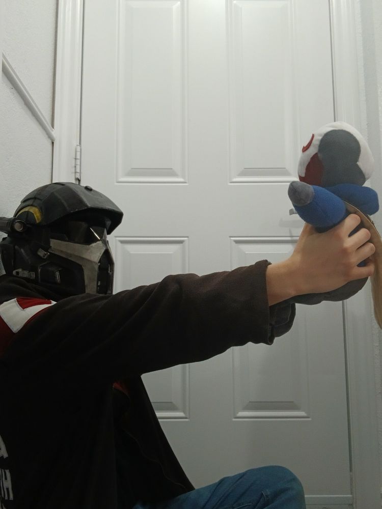 A person wearing a helldiver helmet and automaton hoodie holds a plush automaton wearing a blue sweater up adoringly