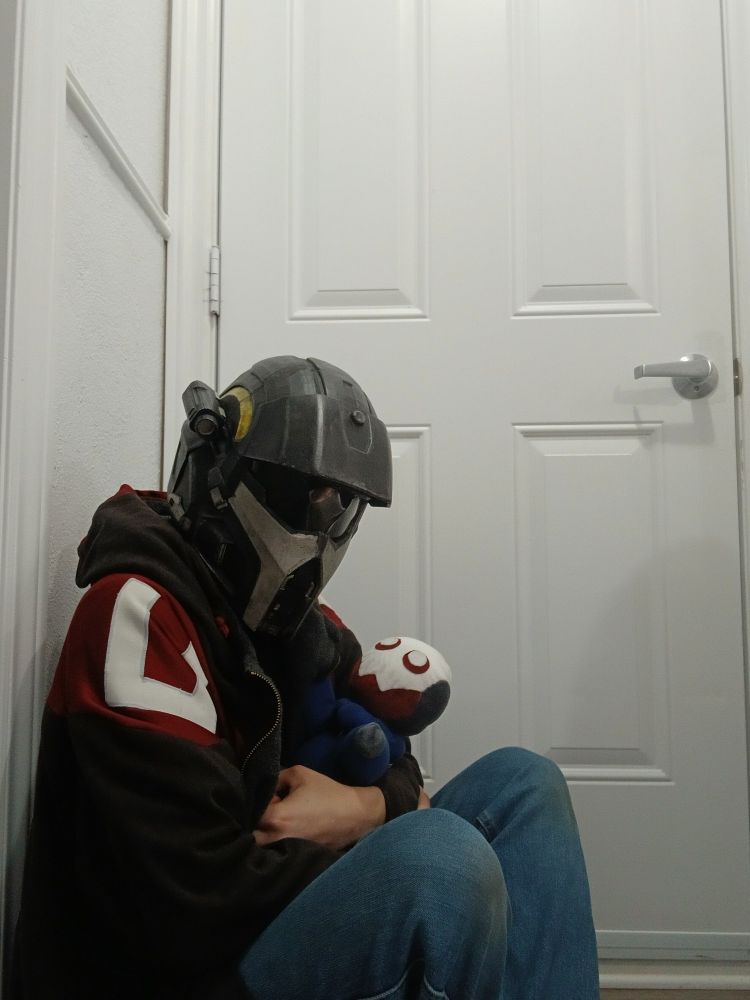 A person wearing a helldiver helmet and an automaton hoodie cradles a plush automaton in their arms