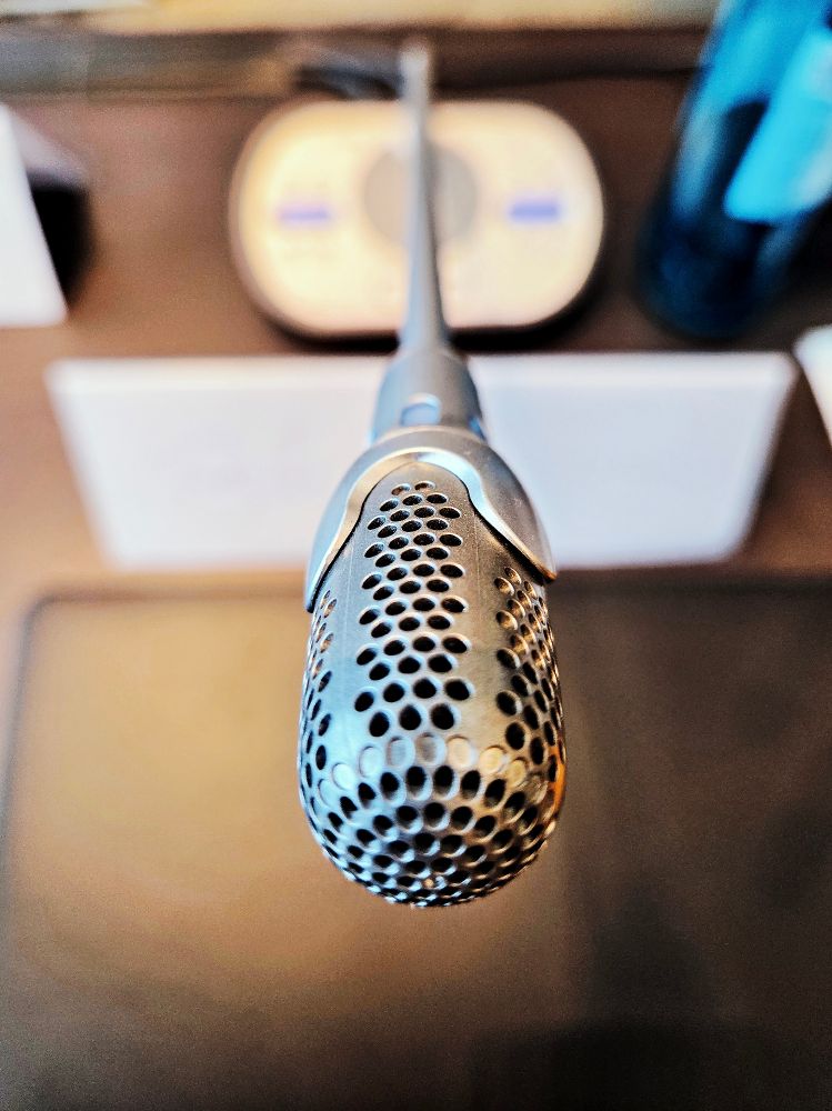 ein Tisch-Mikrofon aus Sicht des Sprechers. Die Schärfe liegt nur auf einem kleinen Bereich des Mikrofon-Kopfes, der gesamte Rest des Fotos ist unscharf.