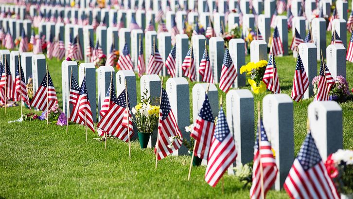 Rows of white headstones adorned with American flags in a military cemetery, honoring fallen soldiers for Memorial Day.