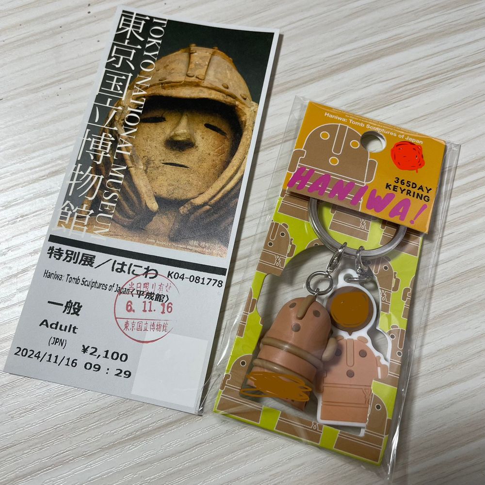 東京国立博物館の特別展のチケットと、物販のお誕生日ハニワキーホルダー。チケットの写真は「挂甲の武人（けいこうのぶじん）」のお顔のアップ、キーホルダーは「踊る人々」の男女がデフォルメされたもの。キーホルダーのモチーフのうち、立体の子はお腹に誕生月が英語3文字で、平面の子は頭上に吹き出しで日付が描かれている。