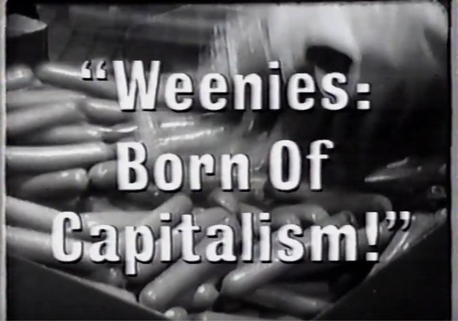 a frame of a advertisement, a black & white picture of hot dogs in a box. It is in a factory with a blur of more weenies conveyor belted into the previously mentioned box. With the text " "Weenies: Born of Capitalism!" " on top of it.