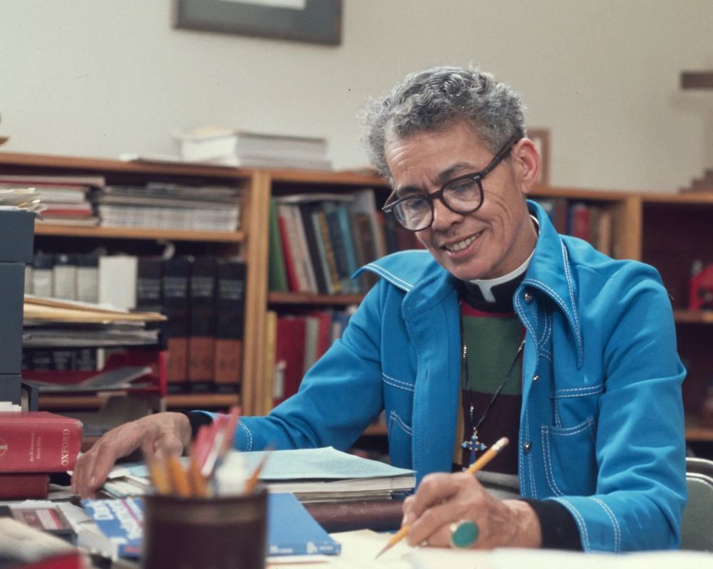 The Rev. Dr. Pauli Murray, scholar, activist, priest, sits smiling at their desk surrounded by a library of books, holding a pencil and absorbed in writing. They wear a clerical collar and a bright blue jacket. 

Pauli was a longtime and tireless civil rights scholar who kept up yearslong correspondence with Eleanor Roosevelt; whose legal theories on sex discrimination deeply influenced Ruth Bader Ginsburg; who was a founder of NOW; and who later in life became the first Black person understood to be a woman to be ordained to the priesthood in the Episcopal Church. Pauli had a woman partner and was also very likely transgender, although they lived ahead of times when the reality of being gay and transgender could be lived out publicly. 

July 1 is the feast day of Pauli Murray in the Episcopal Church’s calendar of saints, Lesser Feasts and Fasts — continuing a celebration of what some folks call Liberation Month in June as we have been celebrating Juneteenth and Pride. 