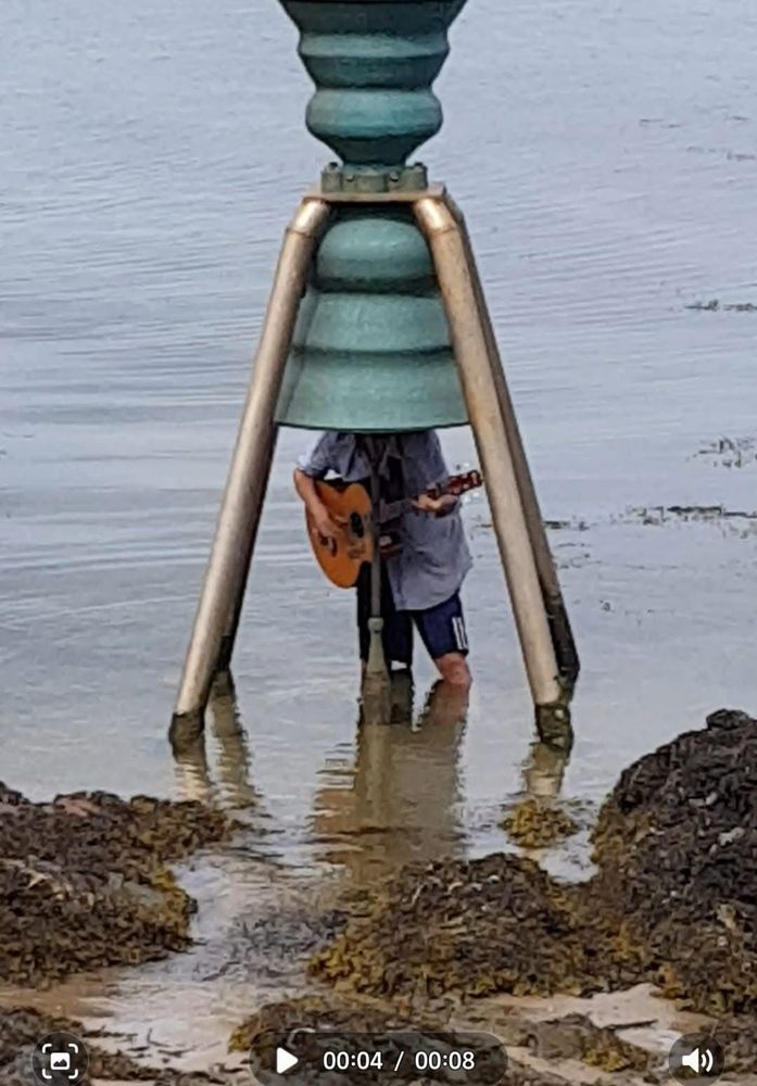 Man playing guitar standing under tide bell