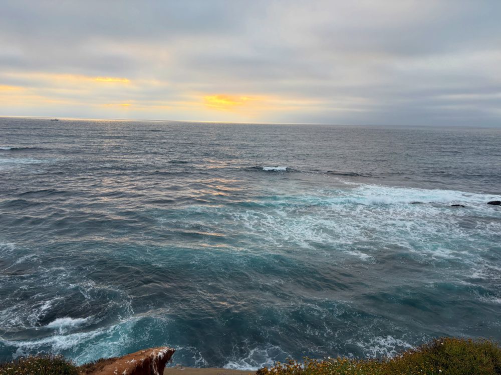 the sun setting over the ocean behind clouds on a grey evening