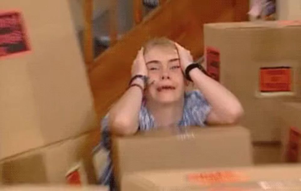 a woman is sitting in front of a box with her hands on her head and making a funny face .