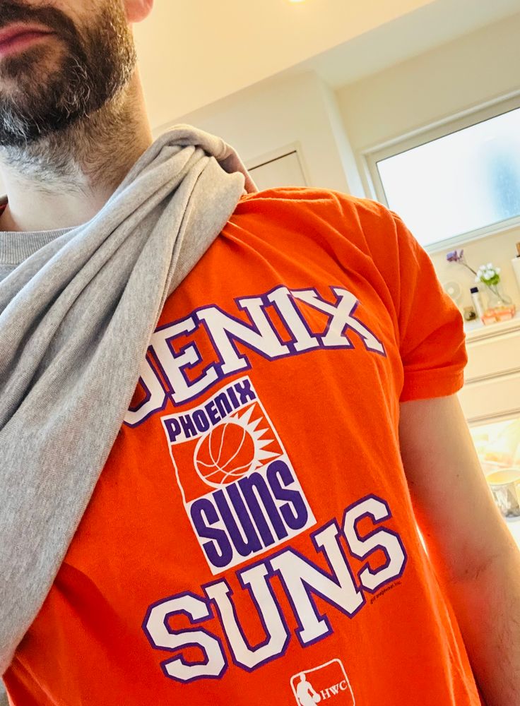 Me wearing an orange phoenix suns t-shirt with a retro logo, a jumper slung over one shoulder. I need to shave