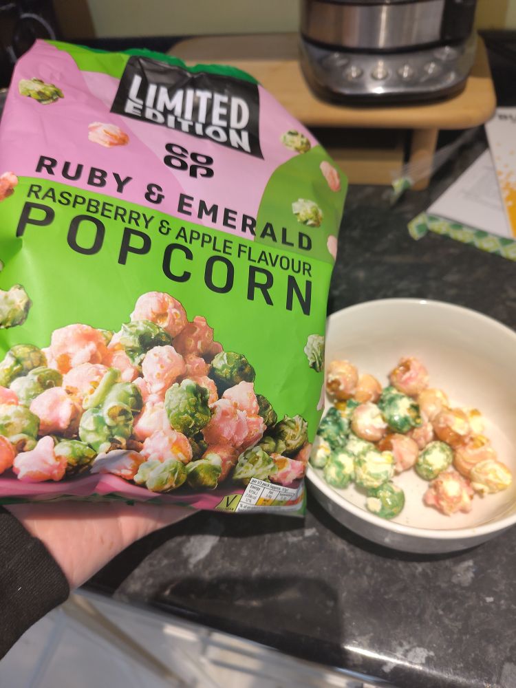 Mike holding a bag of raspberry and apple flavour popcorn next to a bag of pink and green popcorn