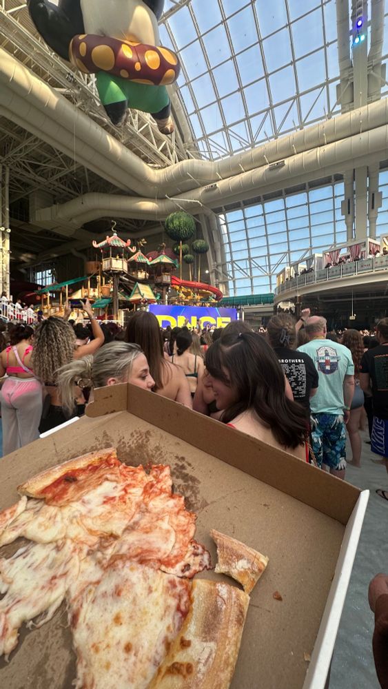 a box of half eaten pizza surrounded by a bunch of people in a pool 