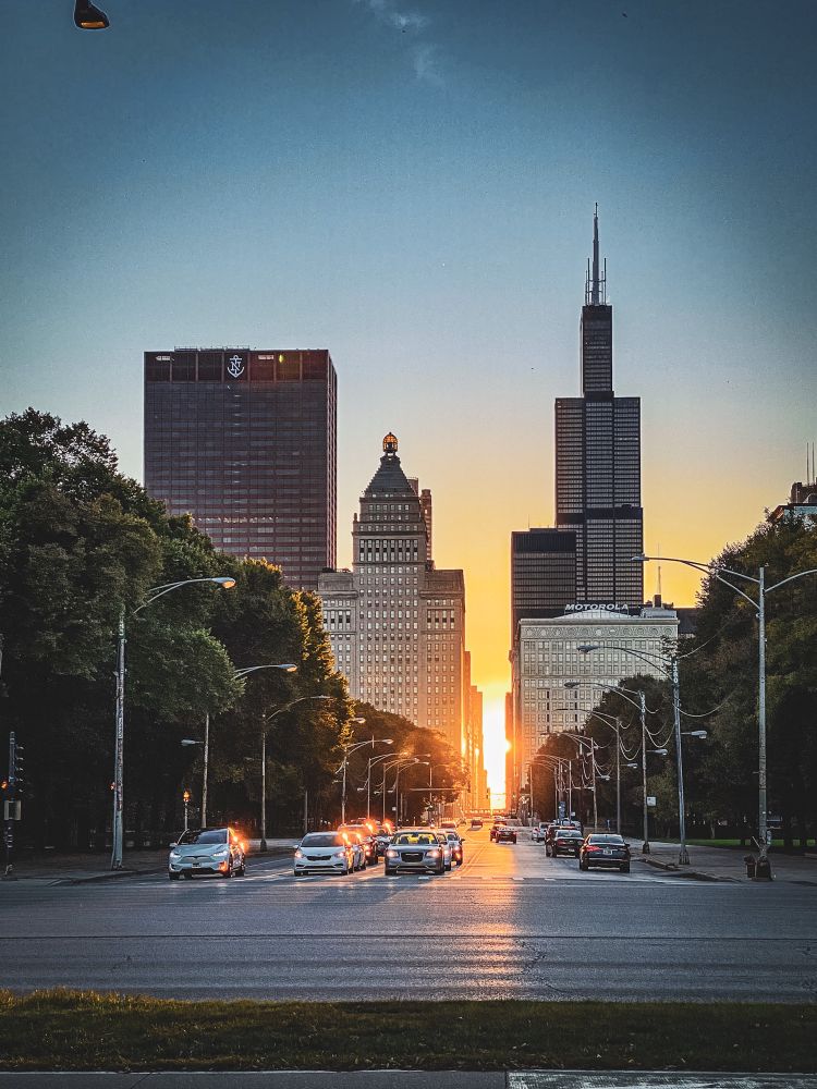 Equinox sun setting through downtown Chicago buildings at an intersection. 