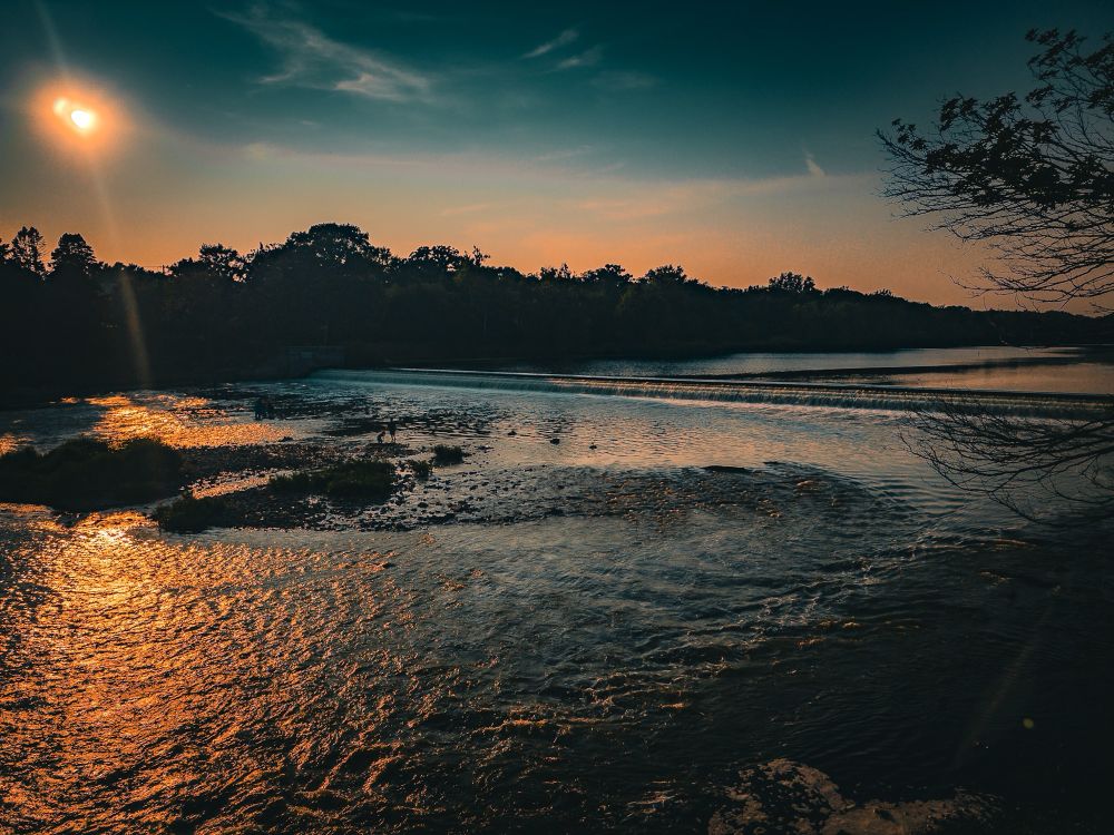 A dam along the fix river in the evening sun. Fisherman cast from an elevation in the shallower part of the river. 
