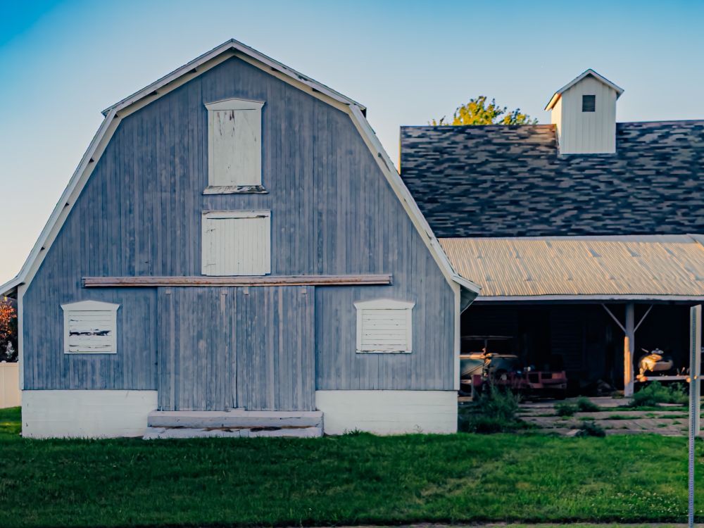 Gray barn-face with a boat in an attached garage with a patch of green grass in front. 